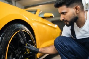 Professional male in overalls and protective gloves, cleaning alloy wheels rims of luxury car